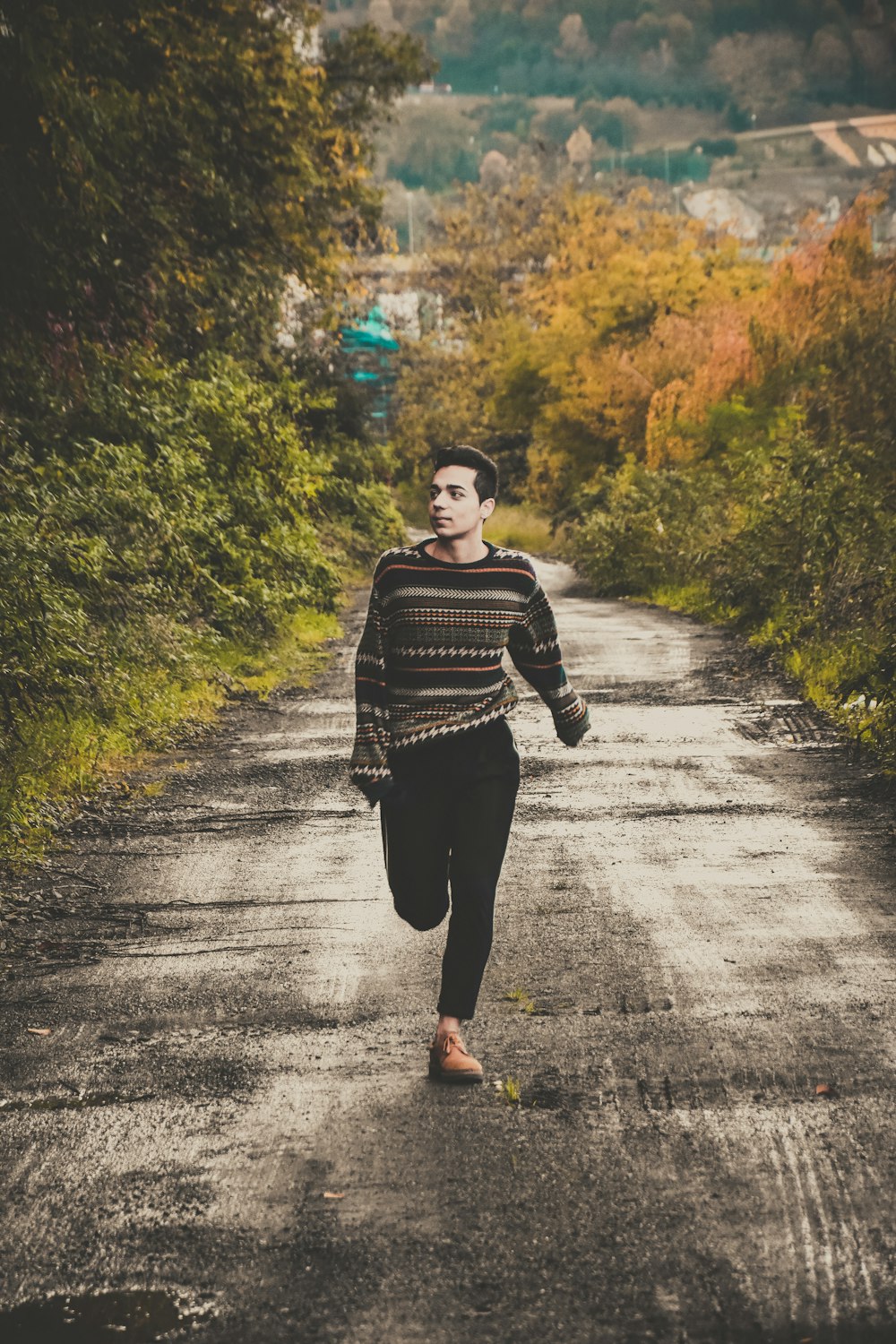 스웨터를 입고 낮에 나무 사이 도로를 달리는 남자
