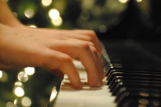 Hands gracefully play the keys of a piano with blurred bokeh lights creating a soft, serene background.