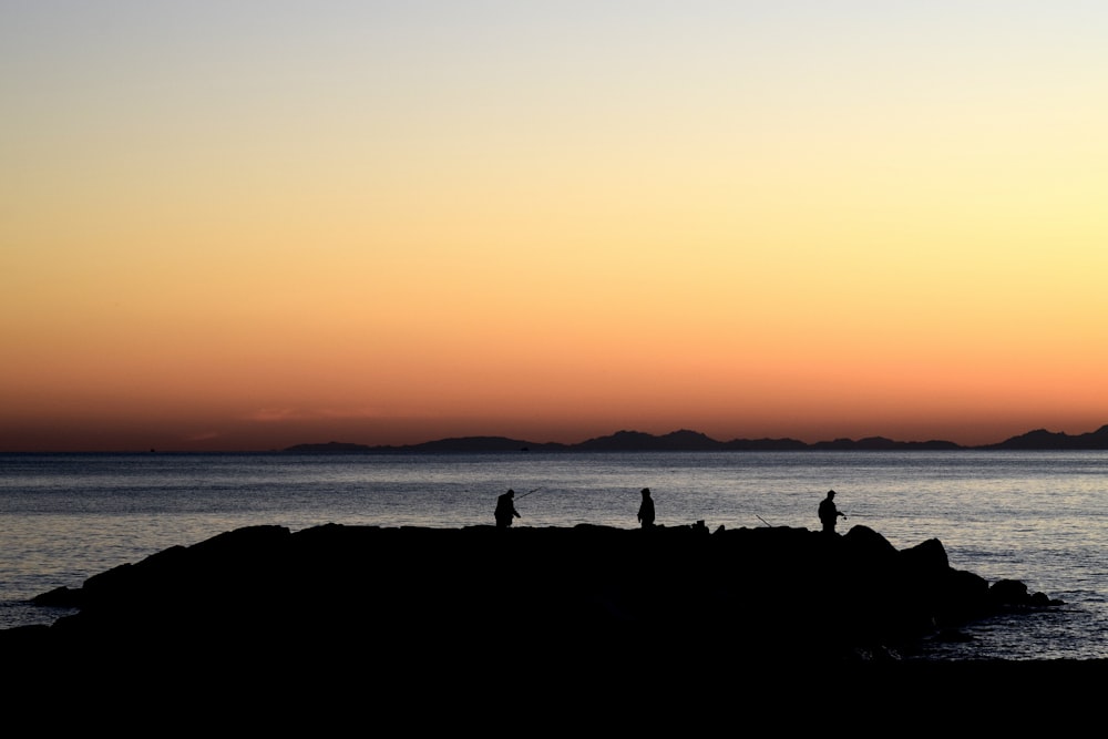 silhouette of three person standing on island during golden hour