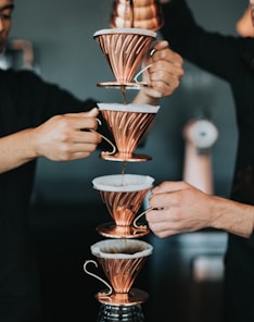 two person pouring coffee with piled cups