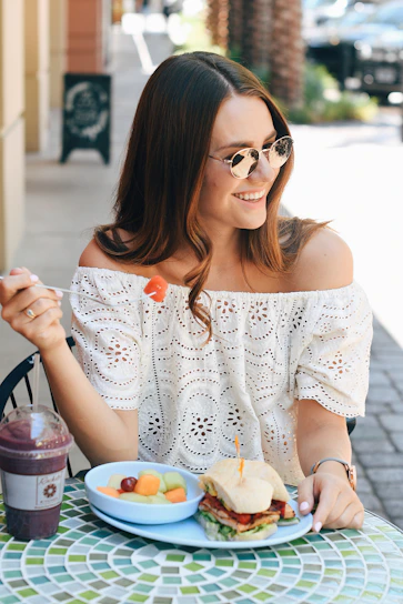 A stylish woman enjoying a sunny brunch with fresh, colorful holistic foods in a light, neutral-toned café.