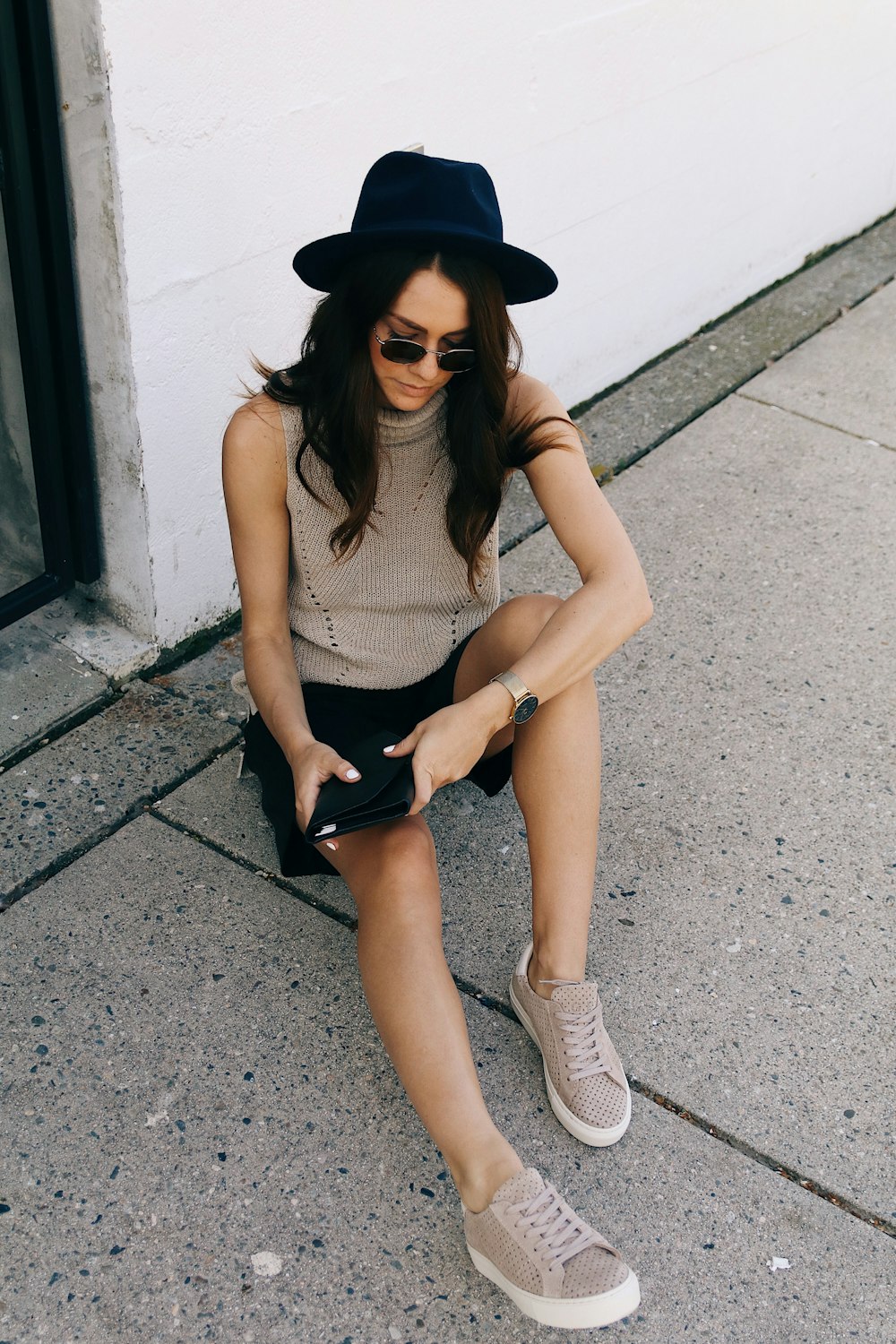 woman sitting on gray concrete pavement beside white wall