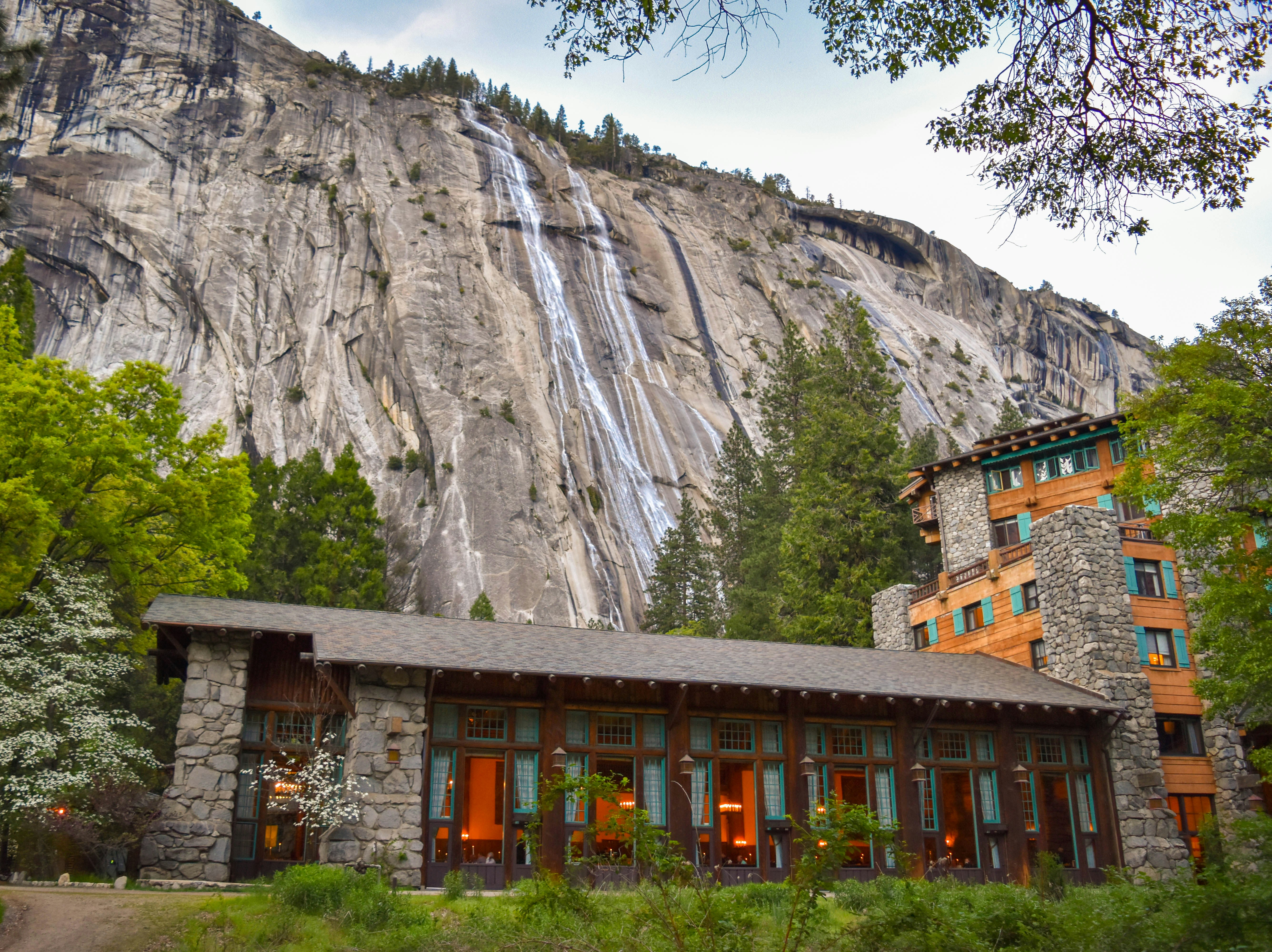building in the foot of the mountain near trees, This is a seasonal waterfall that spills down the face of the Royal Arches wall in Yosemite Valley. I was there on May 5-6, 2017 right after the major winter rain storms. I had never seen the rivers and waterfalls roaring as much as they were on that trip.