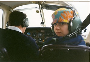 A child taking their first solo flight in a small aircraft, with an instructor watching proudly from the ground.