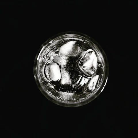 A close-up of crystal-clear gourmet ice cubes melting in a glass of sparkling water branded with vidama's logo.