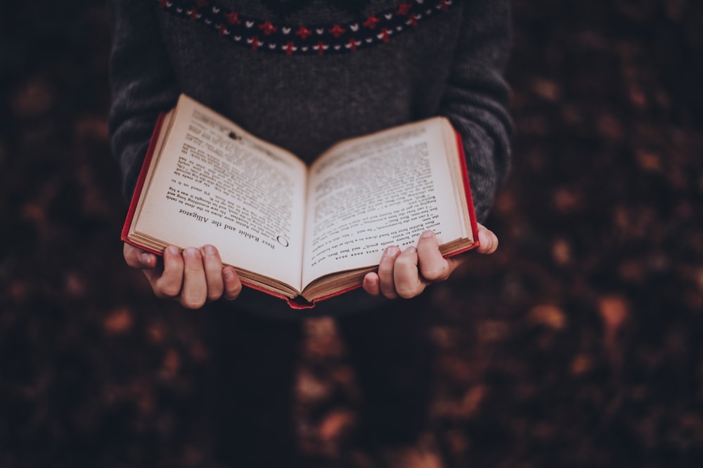 person reads book while standing on leaves