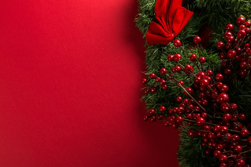 赤い背景に、赤い実とリボンをあしらったクリスマスリース