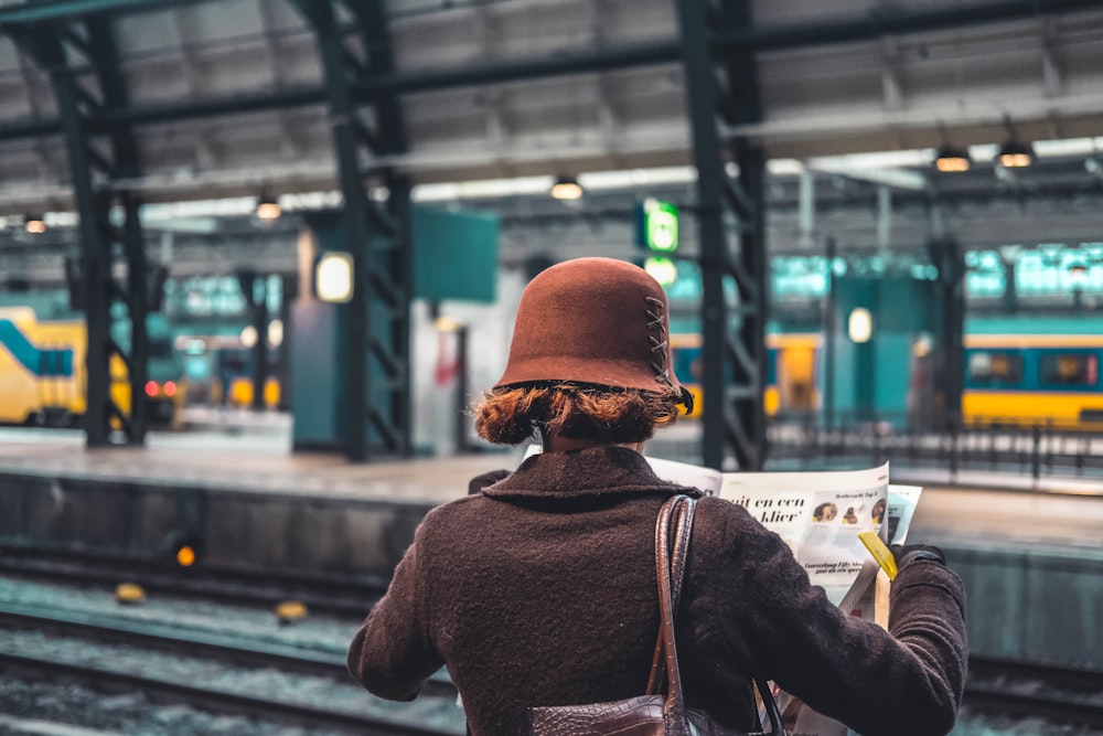 電車のレールの脇で新聞を手にする女性