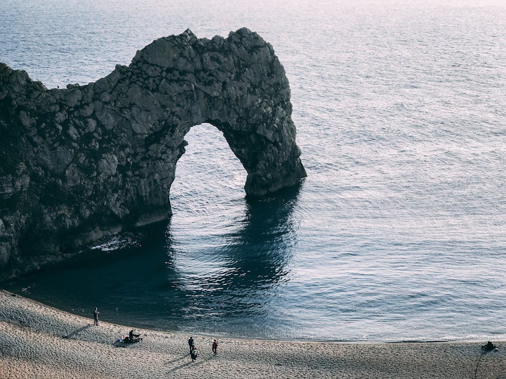 four persons standing on seashore near rock form of arch