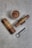 A cup of frothy coffee is placed on a textured surface alongside three cigars neatly wrapped in decorative bands and arranged in a row. A sleek metal cigar cutter with a ring handle lies nearby, suggesting a theme of relaxation and luxury.