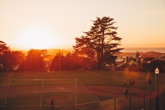 A bright sunset over a community park filled with families.