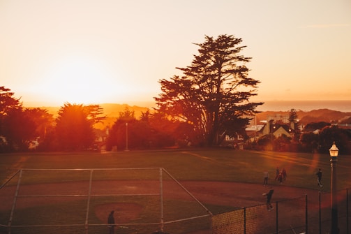 A bright sunset over a community park filled with families.