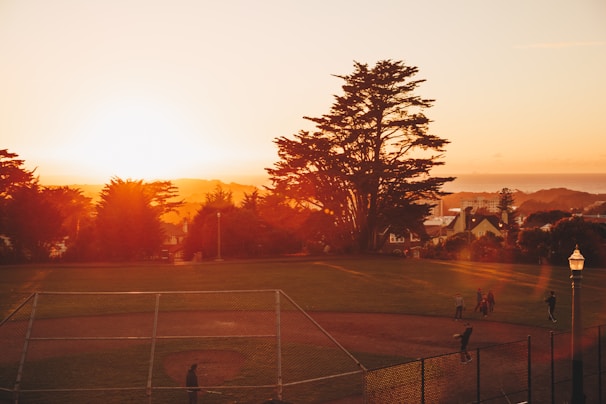 A sunset view over the baseball field where a clinic is wrapping up, with players and coaches packing up gear.