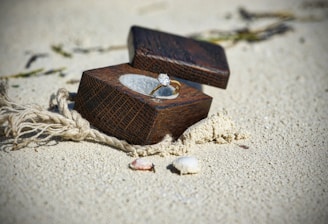 Close-up of a personalized wooden gift box with surf motifs, resting on sandy beach with seashells.
