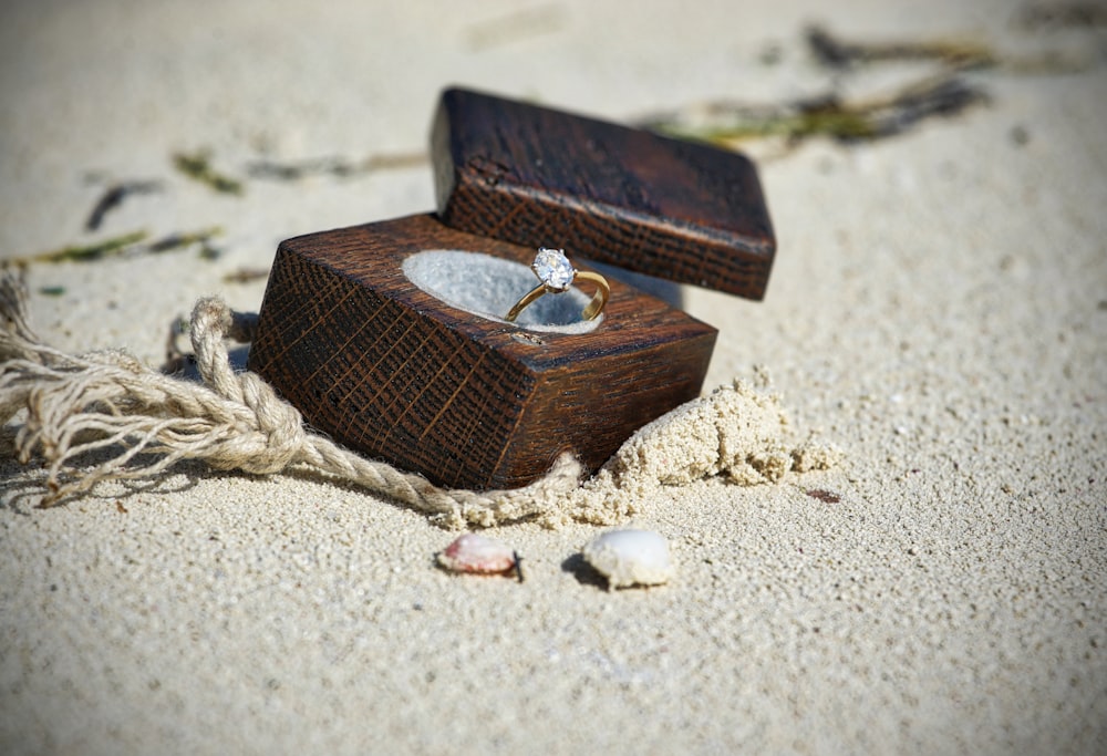 anillo de piedras preciosas transparentes de color dorado en caja de madera marrón sobre arena