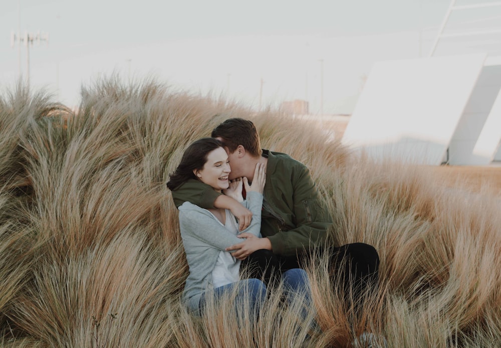 man whispering on womans ear on brown grass field