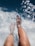 A pair of legs with feet immersed in clear, sparkling water with sunlight reflecting off the surface, creating a relaxing and refreshing scene.