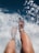A pair of legs with feet immersed in clear, sparkling water with sunlight reflecting off the surface, creating a relaxing and refreshing scene.