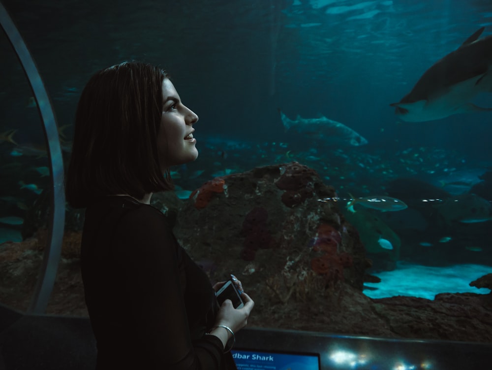 mulher vestindo camisa preta de manga comprida de frente para o aquário