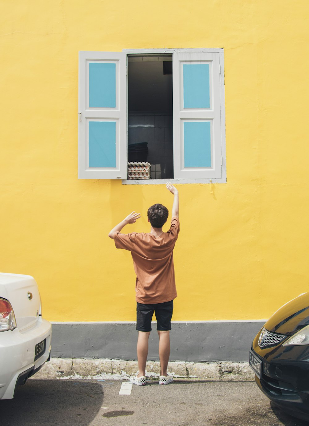 boy in front of window raising hand during daytime