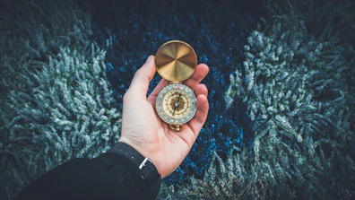 Close-up of hands holding a compass with a navy blue and gold nautical map underneath.