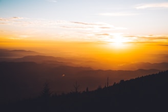A warm, inviting photo of a traveler gazing at a breathtaking sunset over a mountain range.