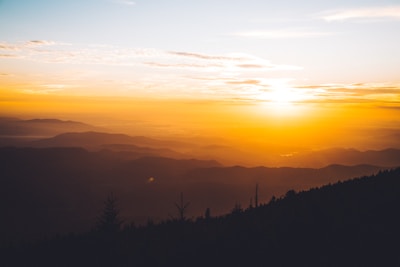 A warm, inviting photo of a traveler gazing at a breathtaking sunset over a mountain range.