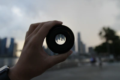 Close-up of a photographer adjusting a camera lens with a cityscape blurred in the background.