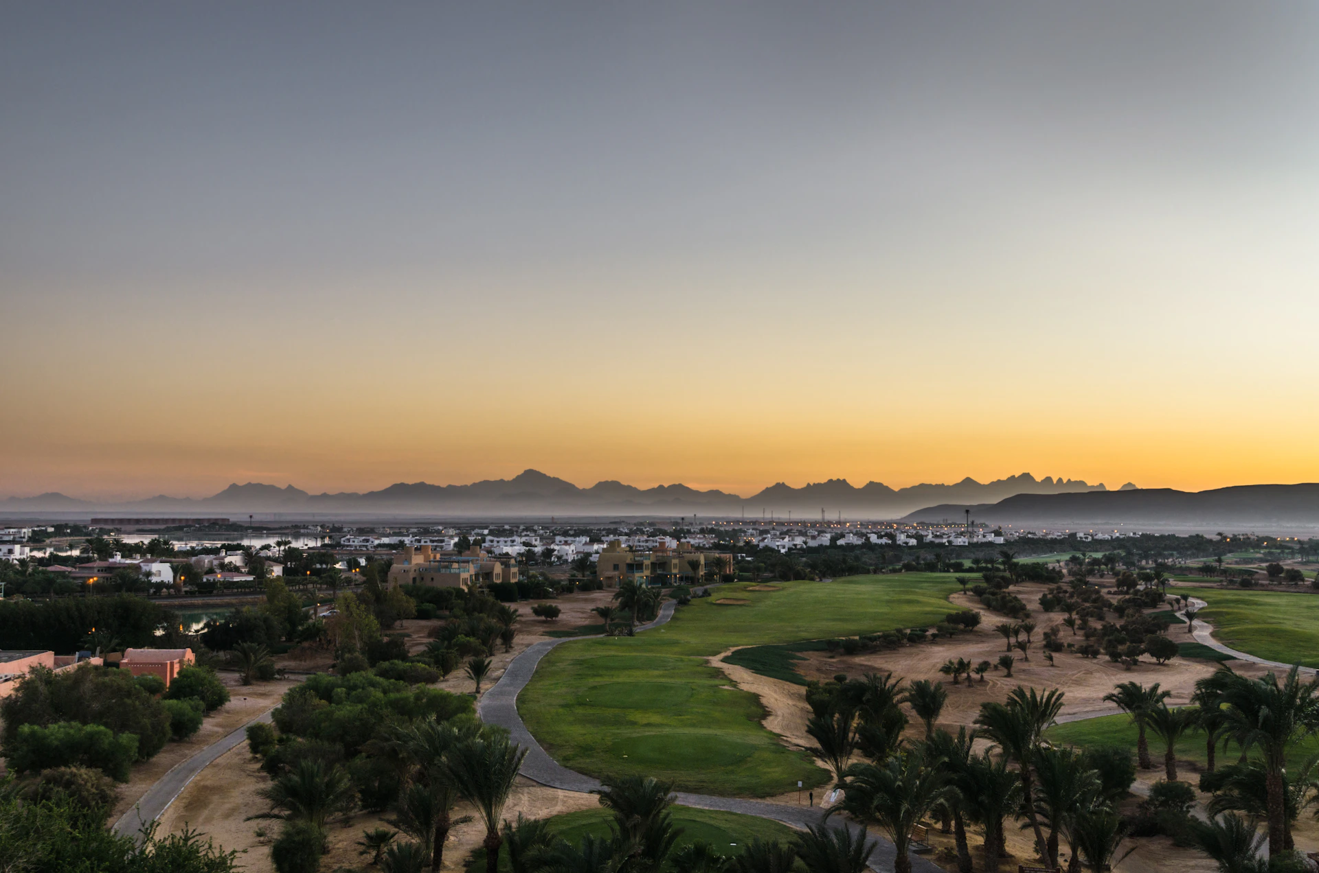 A panoramic view of a sunlit golf course in Murcia with players teeing off under a clear blue sky.