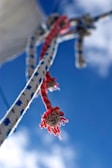 A close-up of a nautical rope with blue and red markings, tied to a structure against a clear blue sky. The ends of the rope are frayed and highlighted by the sunlight, adding texture and detail to the image.