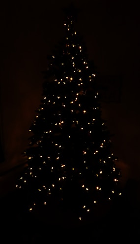 A 3D LED figure of a Christmas tree glowing warmly in a dark room.