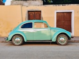 teal Volkswagen Beetle parked near brown house