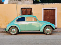 teal Volkswagen Beetle parked near brown house