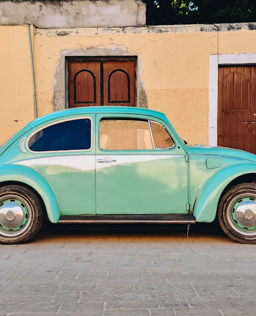 teal Volkswagen Beetle parked near brown house