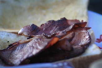 A close-up of crispy, browned slices of bacon resting on a slice of bread, with a blurred background.