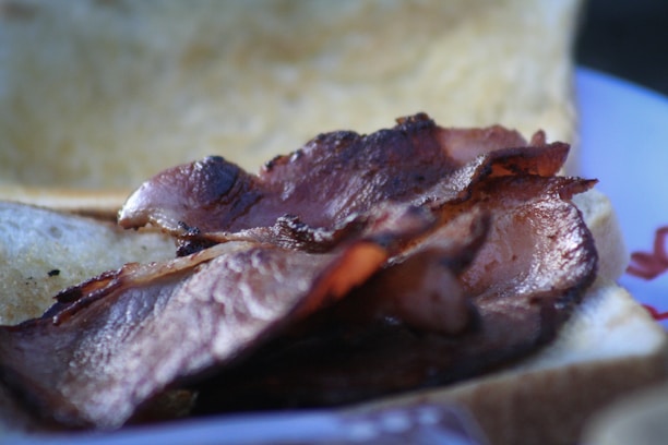 A close-up of crispy, browned slices of bacon resting on a slice of bread, with a blurred background.