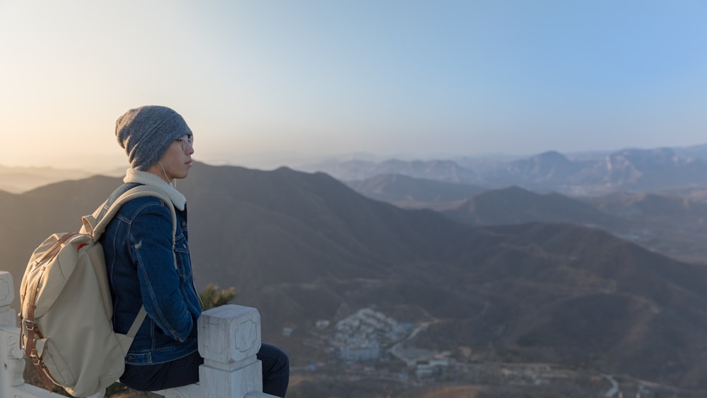 woman sitting on wooden fence overlooking building background of mountain at daytime