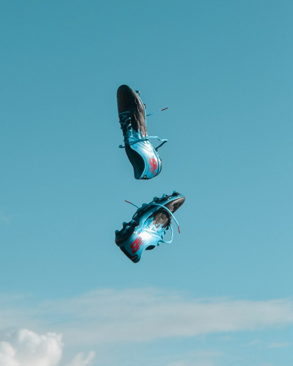 par de tacos New Balance azules y negros en el aire bajo un cielo verde azulado con nubes blancas