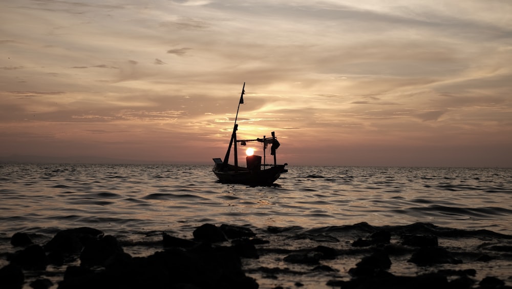 silhouette of boat on body of water with sunset