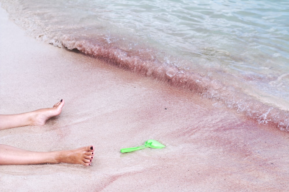 person's foot beside green shovel on seashore