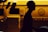 A silhouette of a person wearing a cap is prominently featured against the backdrop of a brightly lit yellow service vehicle with the word 'ROSEG' partially visible and a globe logo. The contrast creates a dramatic interplay between light and dark.