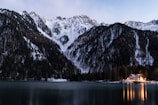 Snow-capped mountains framing a cozy lodge with warm glowing windows at dusk.