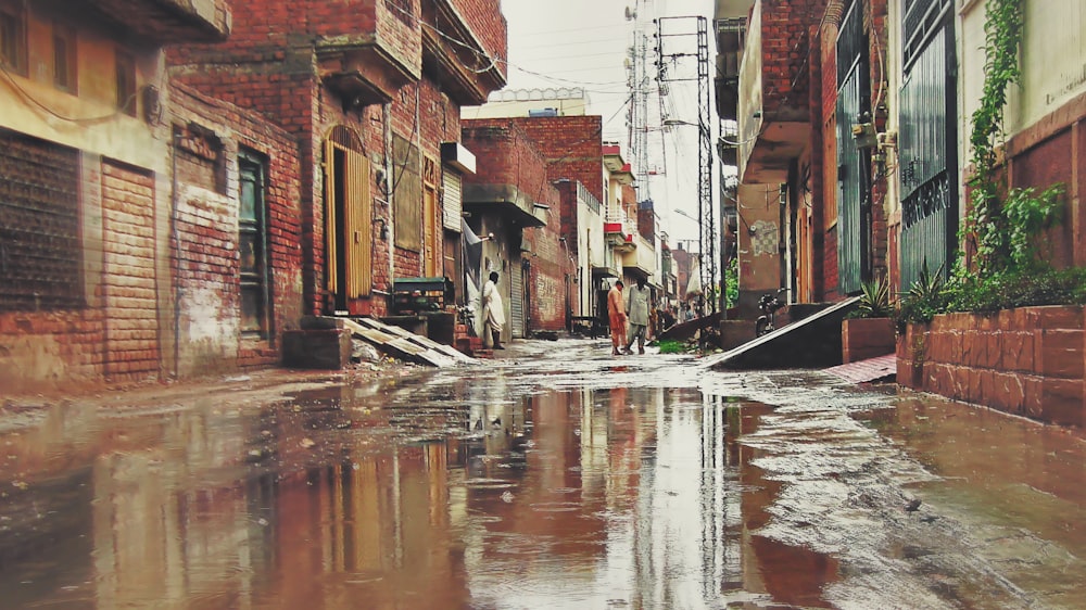 three men walking on mud road between buildings