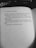A black and white photograph of an open book. The visible page contains text, including the author's name 'Charlaine Harris' and part of a narrative about feelings of loneliness and rejection. A portion of black fabric with white lettering is partially visible at the top.