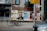 A street scene features a bicycle parked on the sidewalk in front of a wall covered with various posters. The posters advertise movies, music events, and beverages. A street sign is visible, indicating the location as Dundas St. W. A car is partially seen in the bottom right corner.