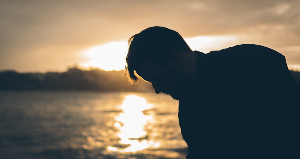 man standing near body of water during sunset