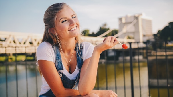 woman wearing white crew-neck shirt holding lollipop near bridge