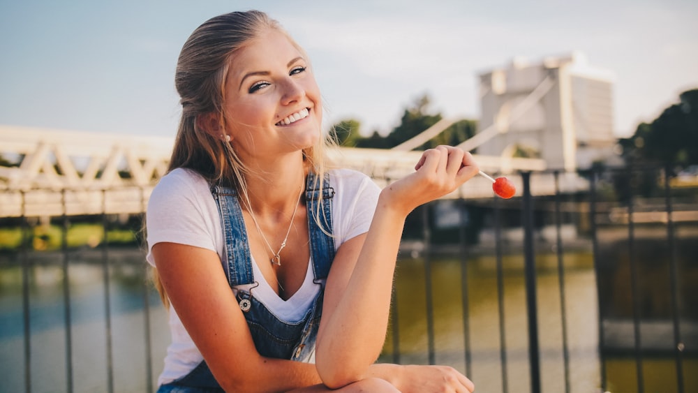 woman wearing white crew-neck shirt holding lollipop near bridge