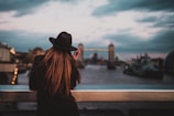 selective focus photo of back of woman wearing fedora hat with elbows on railings facing bridge