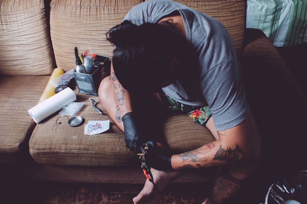 hombre sentado en el sofá haciendo una sesión de tatuaje